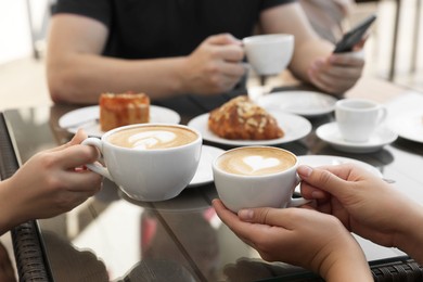 Photo of Friends drinking coffee at wooden table in outdoor cafe, closeup