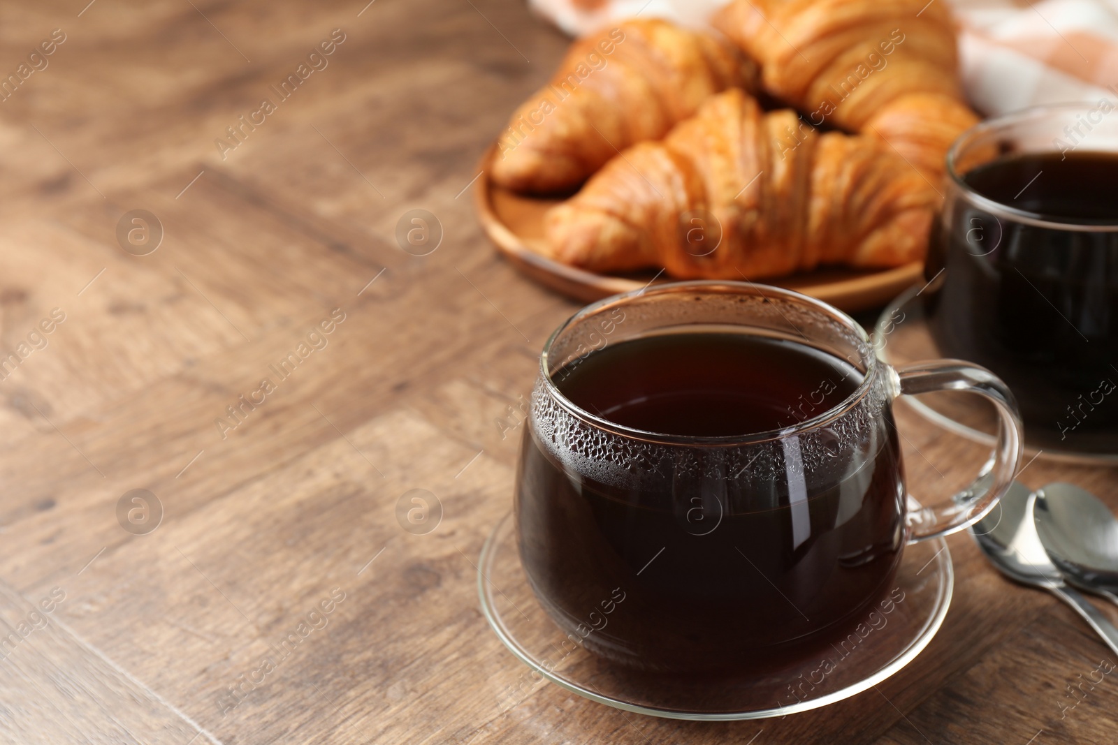 Photo of Hot coffee in glass cup on wooden table, closeup. Space for text