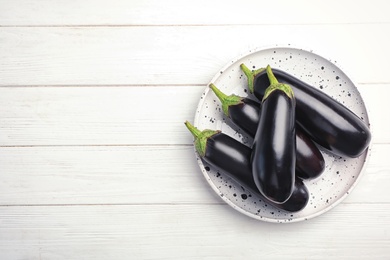 Photo of Plate with raw ripe eggplants on wooden background, top view