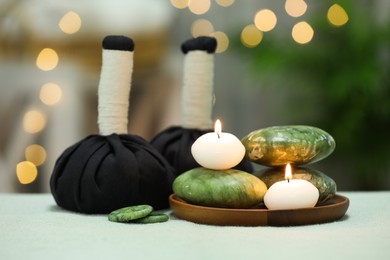 Photo of Spa composition. Herbal massage bags, stones and burning candles on white towel against blurred lights