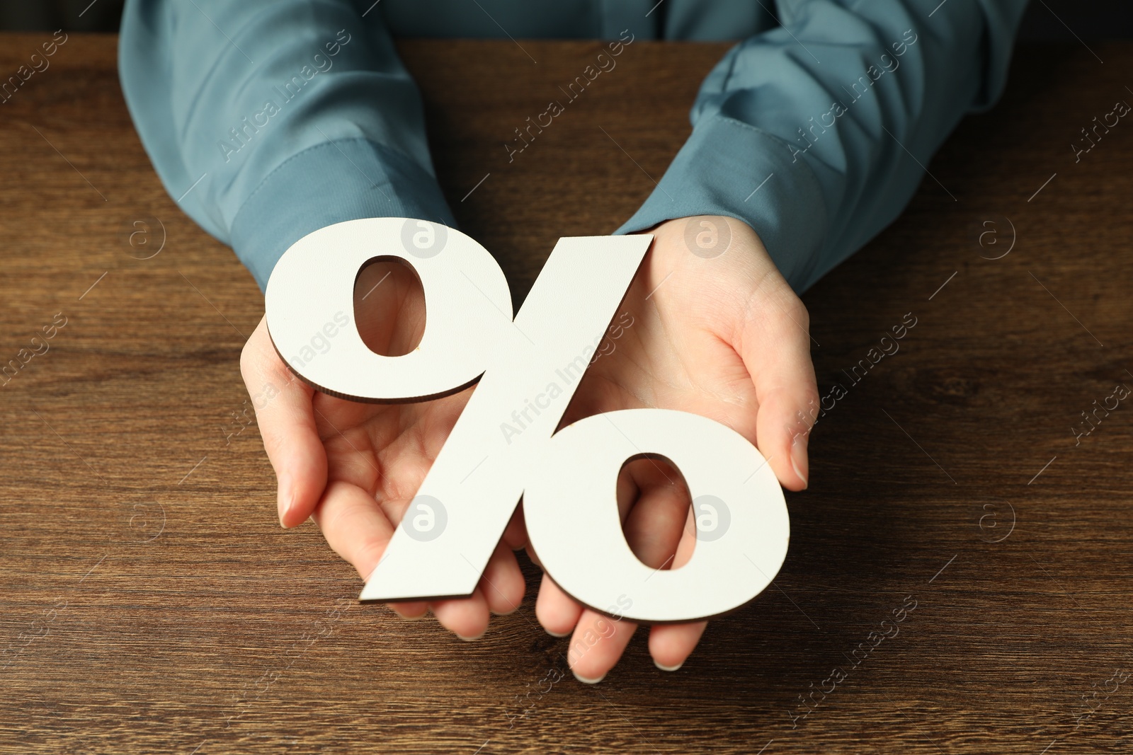 Photo of Woman holding percent sign at wooden table, closeup