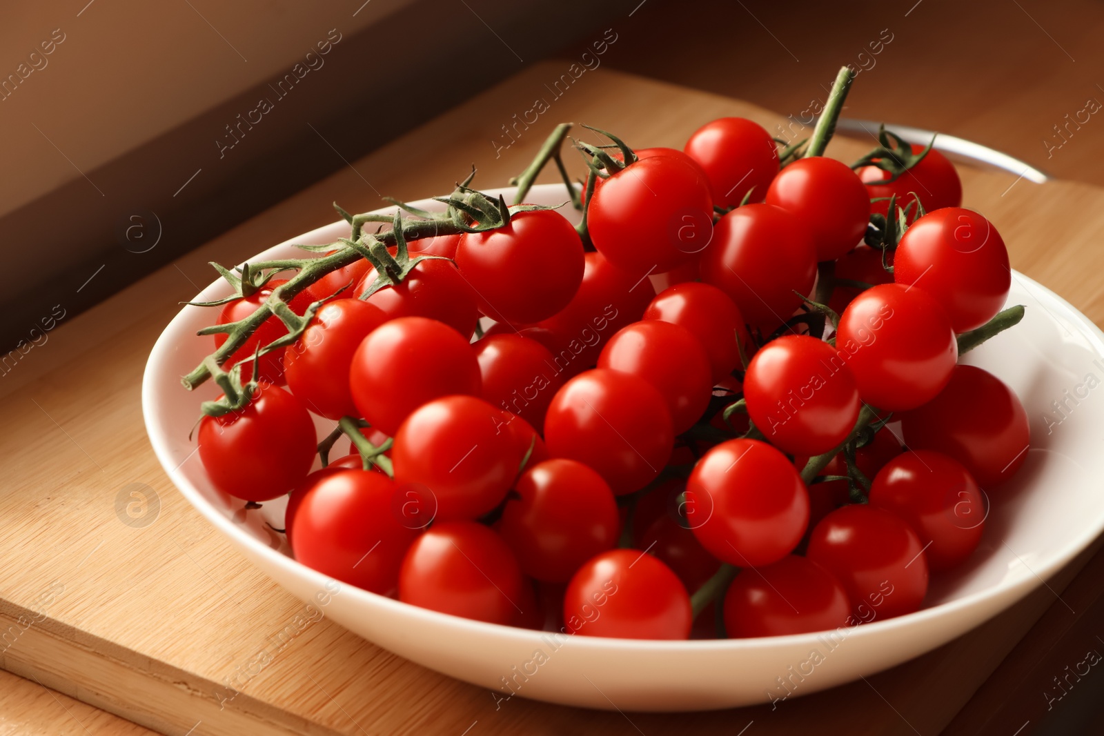 Photo of Plate of ripe whole cherry tomatoes on wooden table, closeup