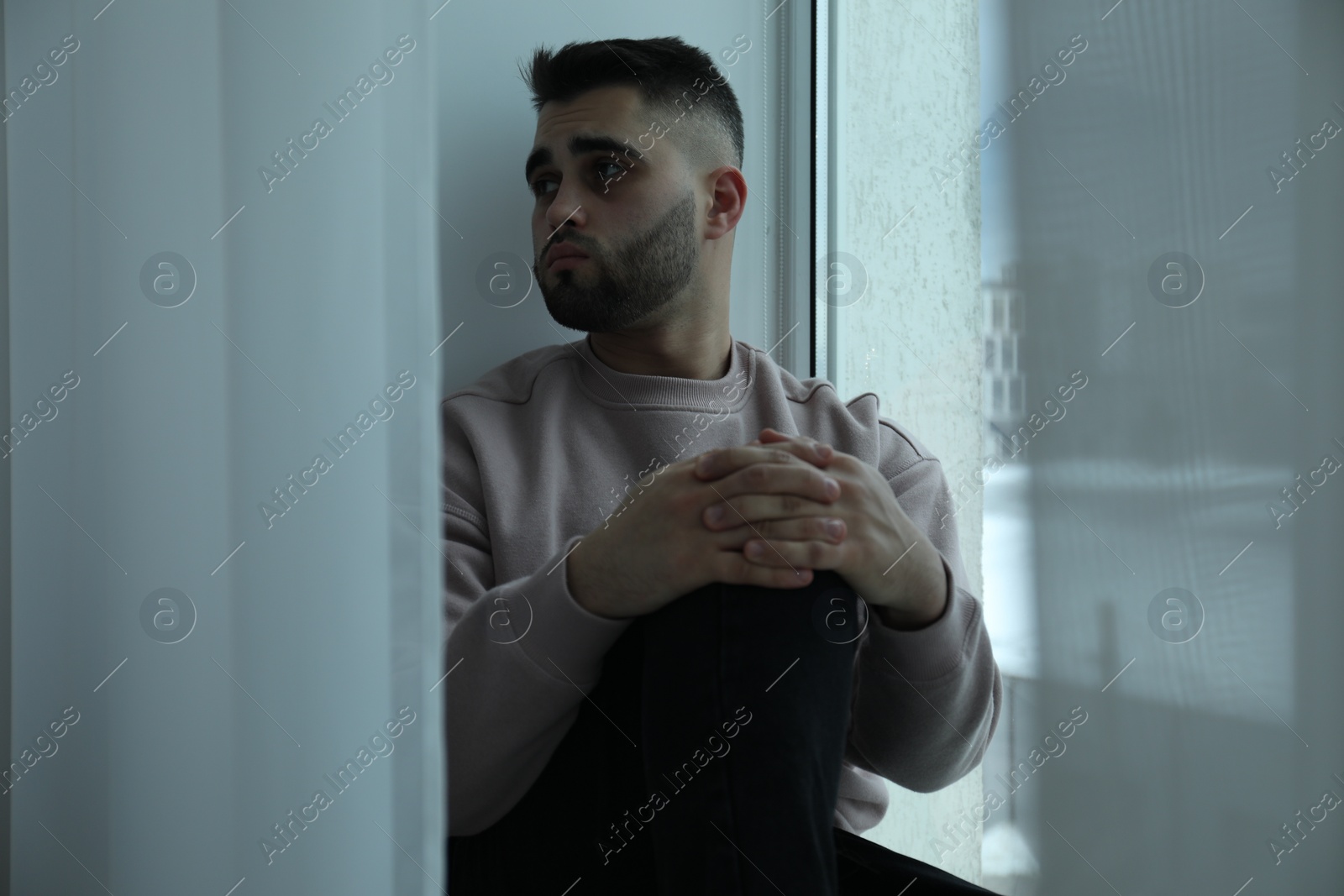 Photo of Sad man sitting near window at home