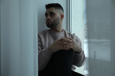 Photo of Sad man sitting near window at home