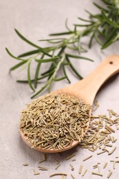 Photo of Wooden spoon with dry rosemary on light grey table, closeup