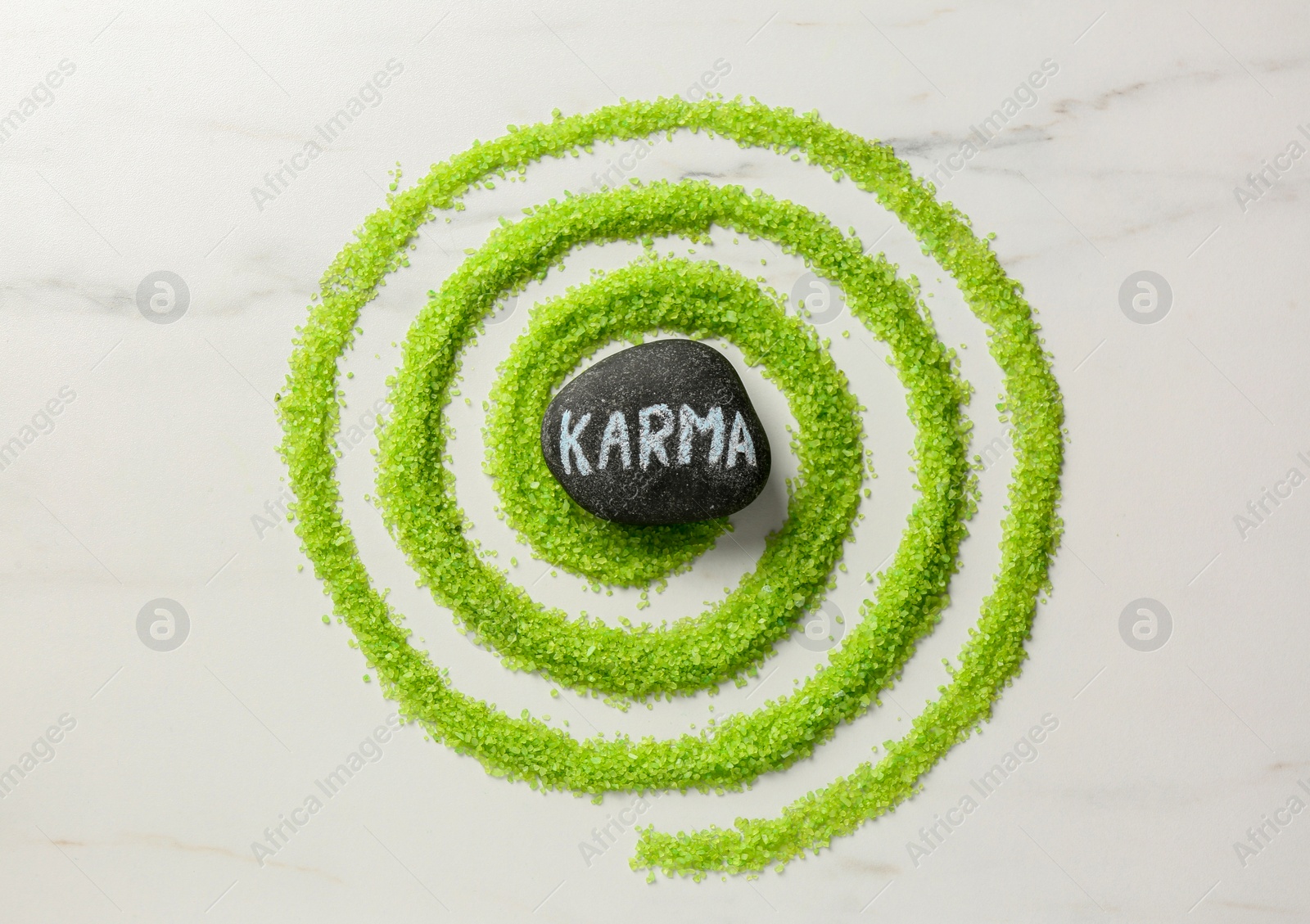 Photo of Stone with word Karma and circle made of light green sea salt on white marble table, top view