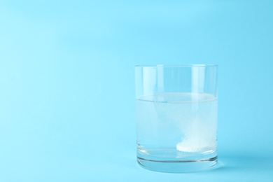 Photo of Glass of water with effervescent tablet on light blue background, space for text