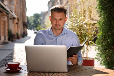 Photo of Handsome man with book working on laptop at table in outdoor cafe