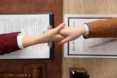 Photo of Notary shaking hands with client at wooden table, top view