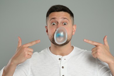 Surprised man blowing bubble gum on light grey background