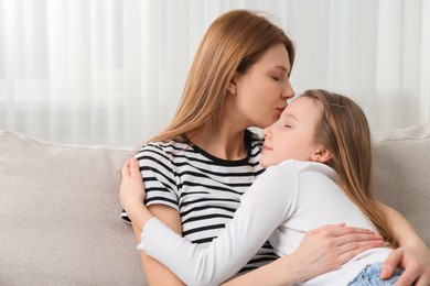Photo of Mother kissing her cute daughter on sofa at home