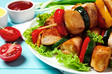 Photo of Delicious chicken shish kebabs with vegetables on light blue wooden table, closeup