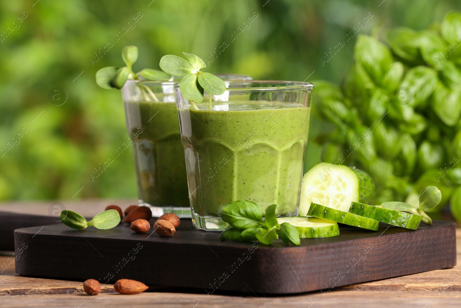 Photo of Glasses of fresh green smoothie and ingredients on wooden table outdoors