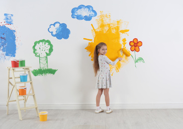 Photo of Little child painting wall with roller brush indoors