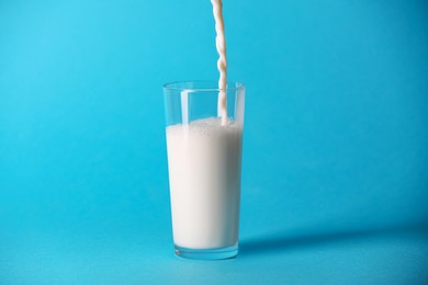 Photo of Pouring fresh milk into glass on light blue background
