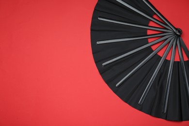 Photo of Stylish black hand fan on red background, top view. Space for text