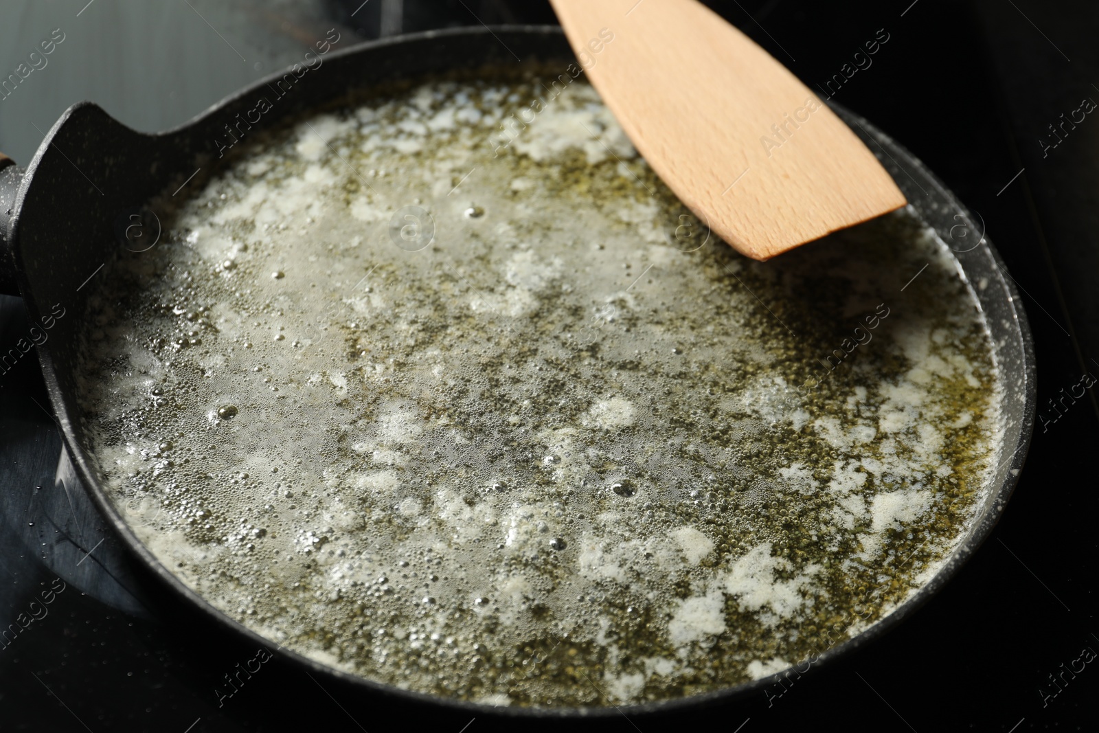 Photo of Melted butter in frying pan and wooden spatula on table, closeup