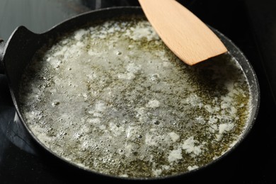 Photo of Melted butter in frying pan and wooden spatula on table, closeup