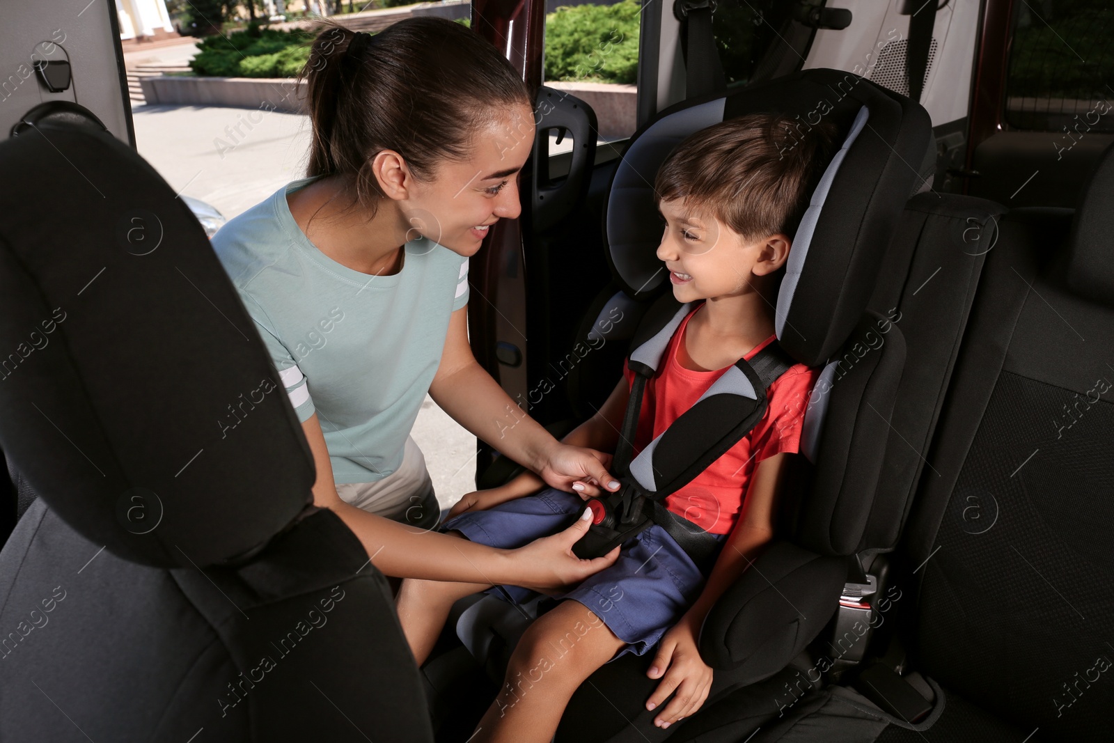 Photo of Mother fastening her son with car safety belt in child seat