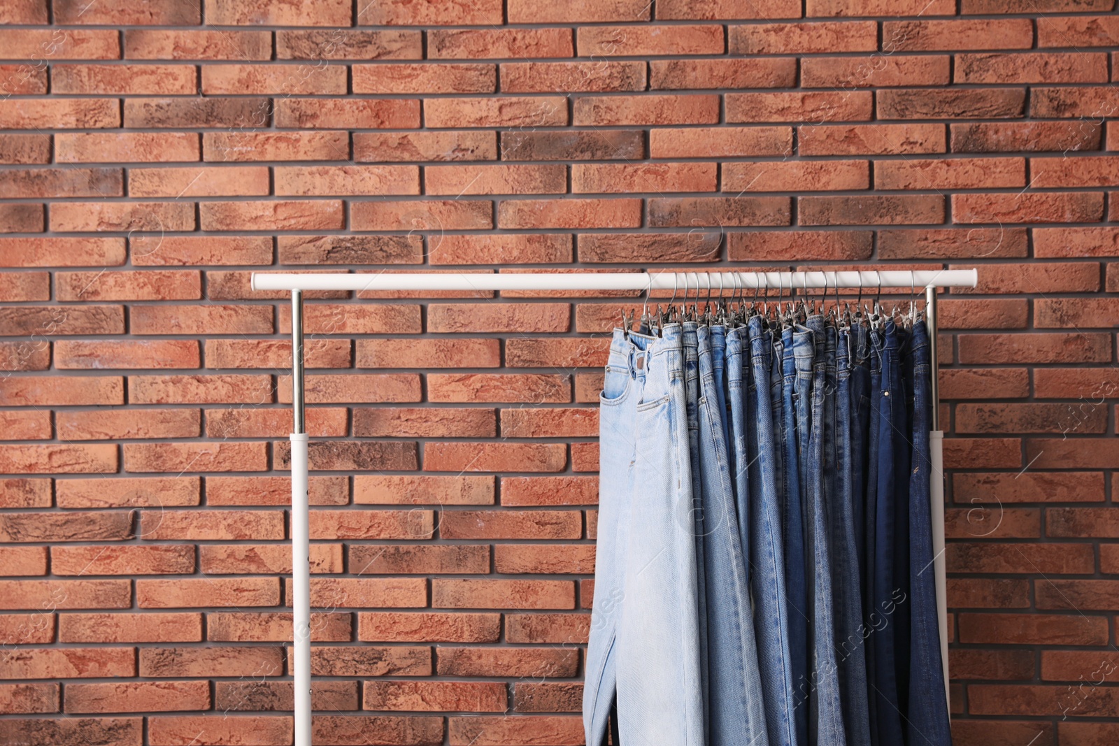 Photo of Rack with stylish jeans near brick wall