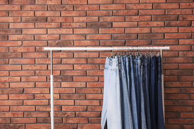 Rack with stylish jeans near brick wall