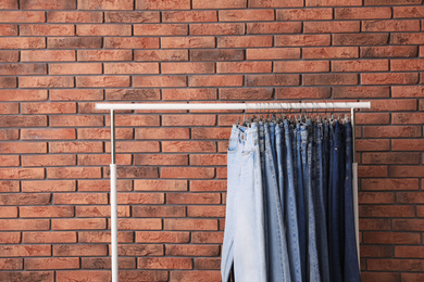 Photo of Rack with stylish jeans near brick wall