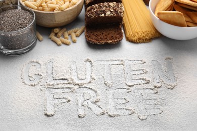 Different healthy products and phrase Gluten Free made of flour on white table, above view