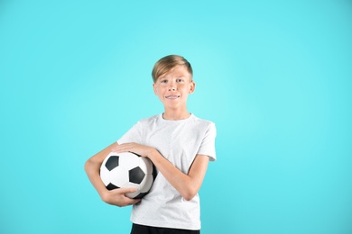 Portrait of young boy holding soccer ball on color background