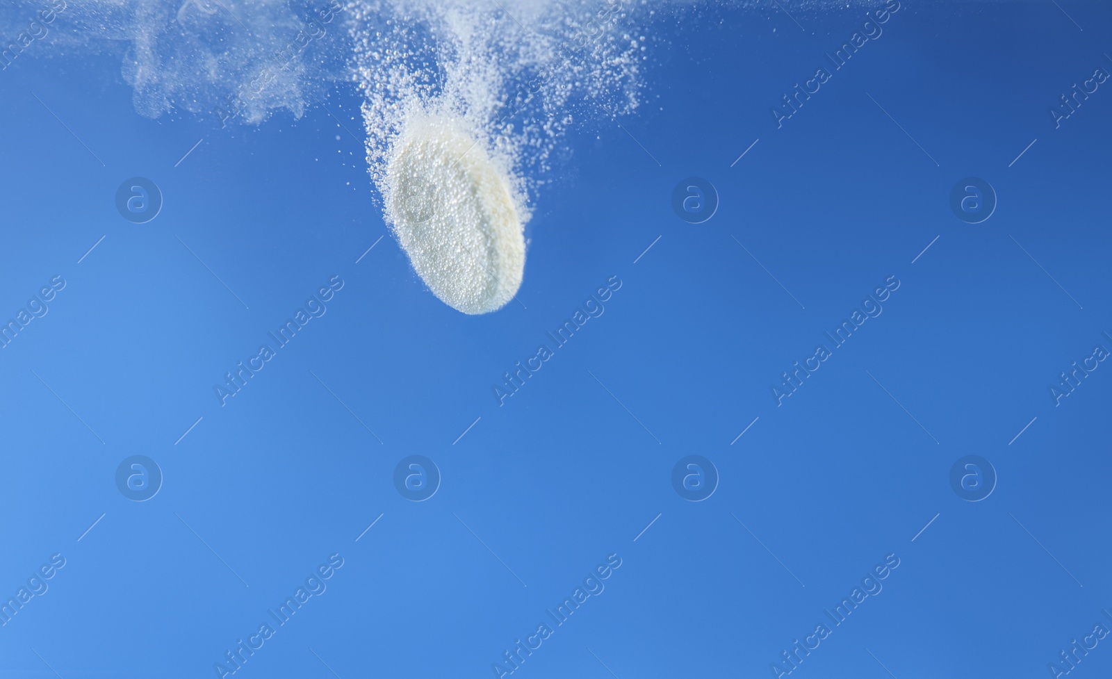 Photo of Effervescent pill dissolving in water on blue background, closeup