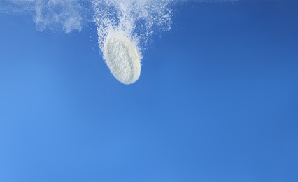 Effervescent pill dissolving in water on blue background, closeup