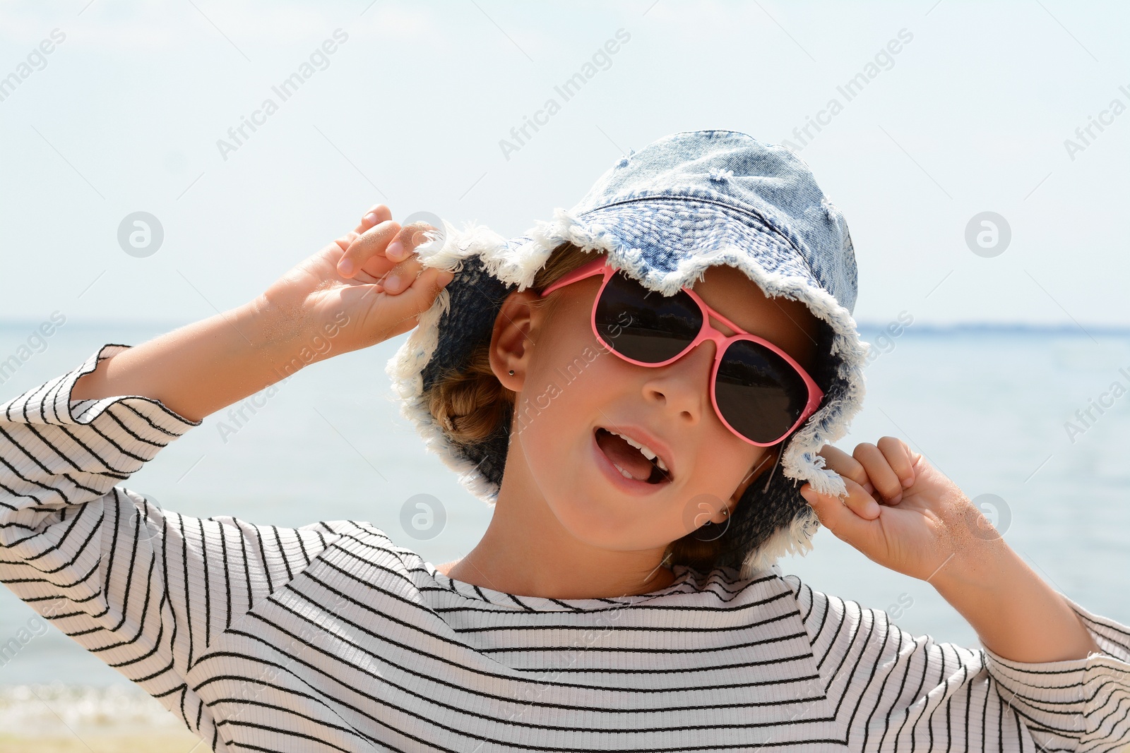 Photo of Little girl wearing sunglasses and hat at beach on sunny day