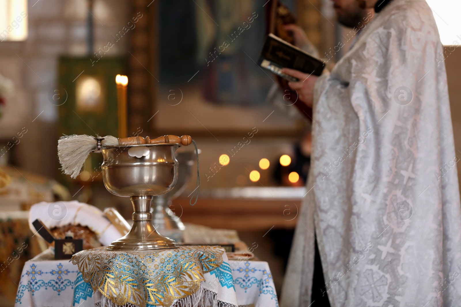 Photo of MYKOLAIV, UKRAINE - FEBRUARY 27, 2021: Priest conducting baptism ceremony in Kasperovskaya icon of Mother of God cathedral, focus on vessel with holy water and brush