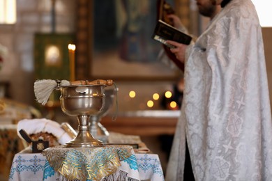 Photo of MYKOLAIV, UKRAINE - FEBRUARY 27, 2021: Priest conducting baptism ceremony in Kasperovskaya iconMother of God cathedral, focus on vessel with holy water and brush