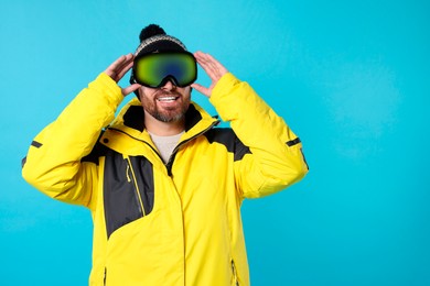 Winter sports. Happy man in ski suit and goggles on light blue background, space for text