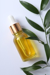 Bottle of cosmetic oil and leaves on white background, flat lay