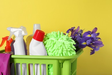 Spring cleaning. Basket with detergents, flowers and tools on yellow background, closeup