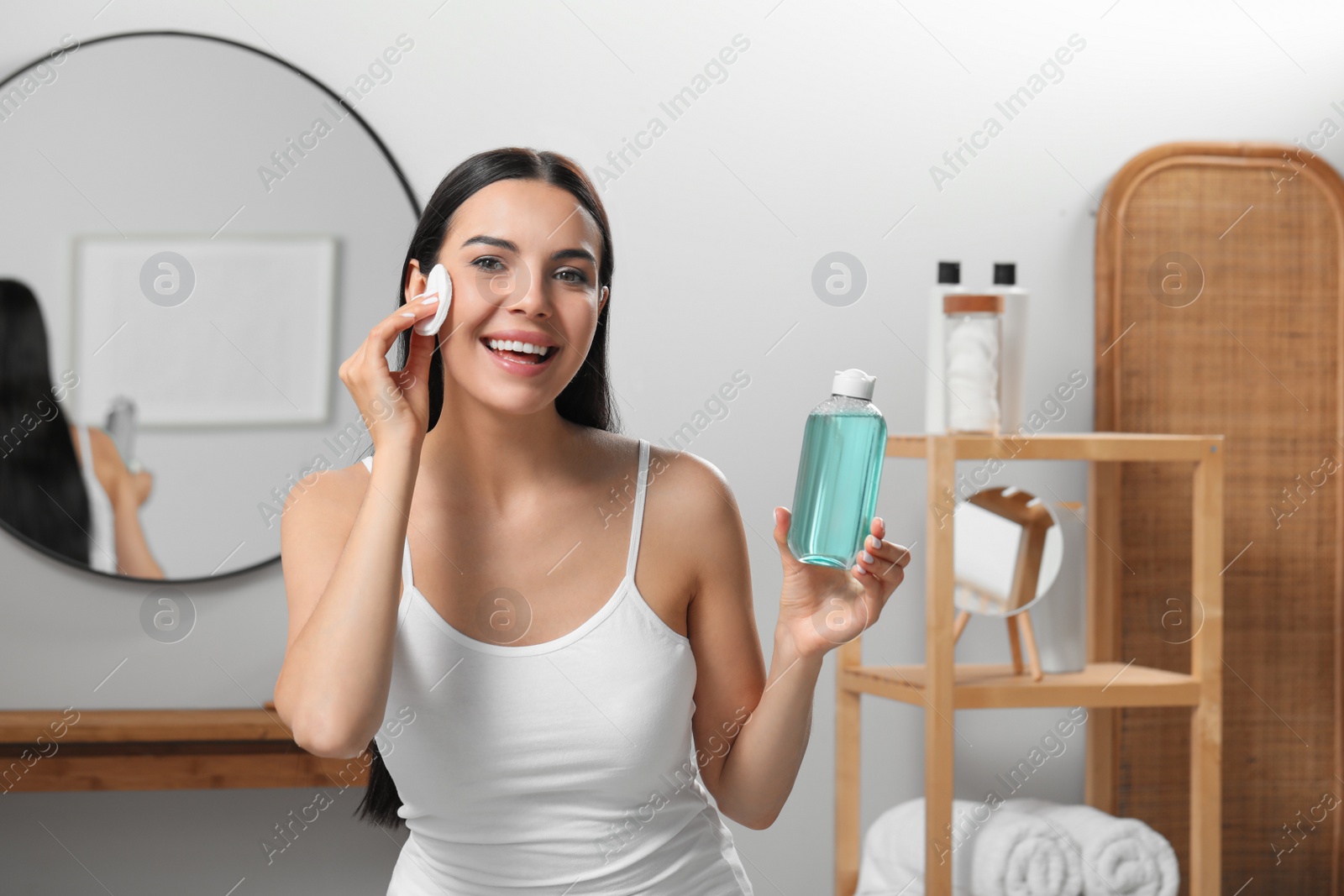 Photo of Young woman using cotton pad with micellar water indoors