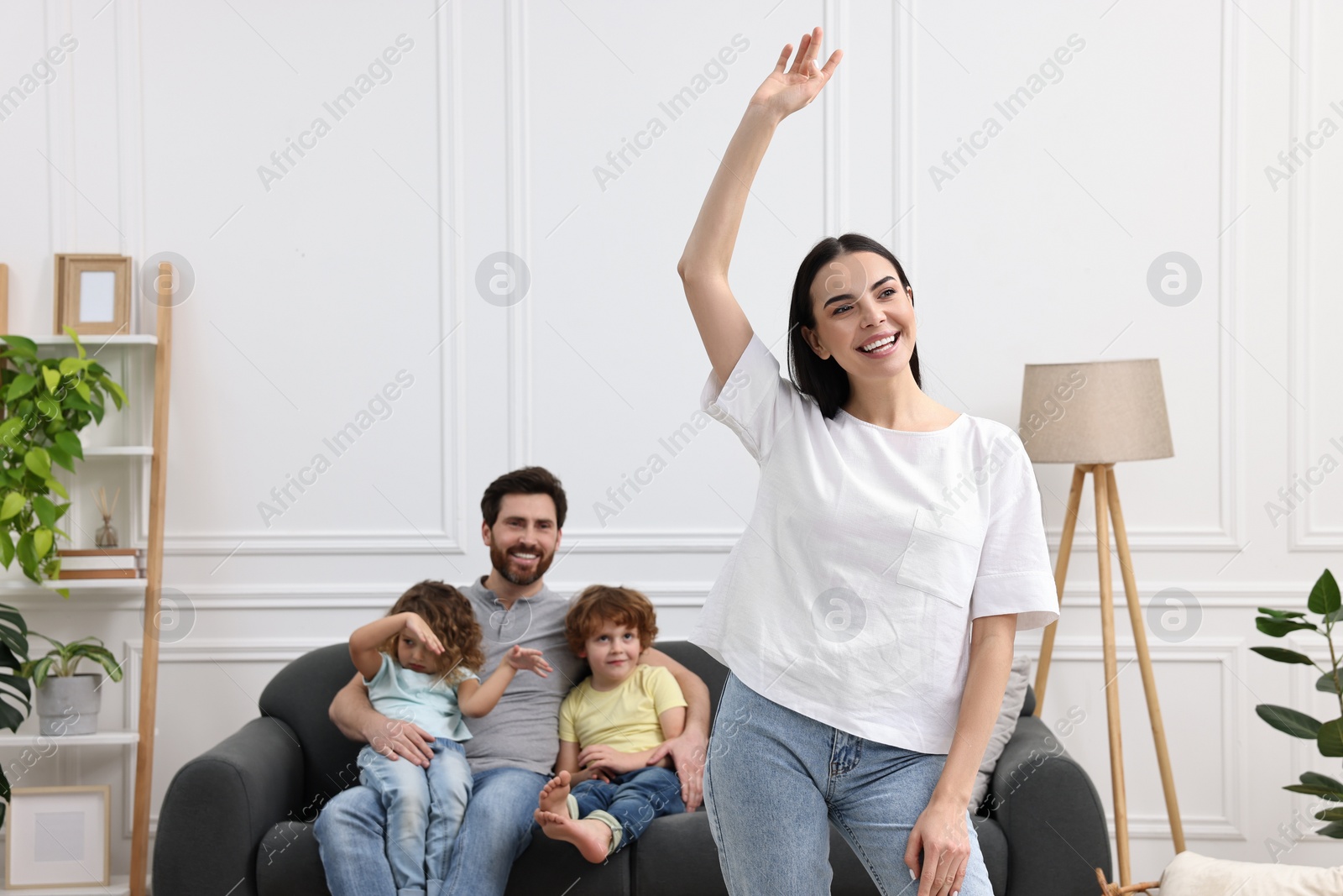 Photo of Happy family having fun at home. Mother dancing while her relatives resting on sofa