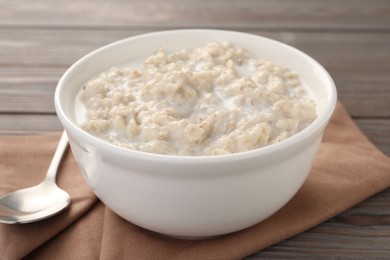 Photo of Tasty boiled oatmeal in bowl and spoon on table, closeup