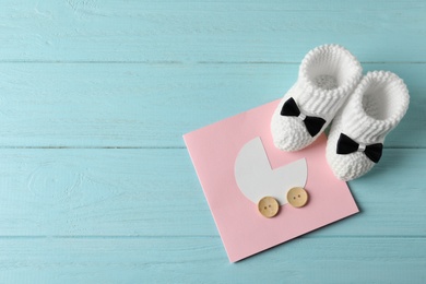 Handmade baby booties and greeting card on wooden background, top view with space for text