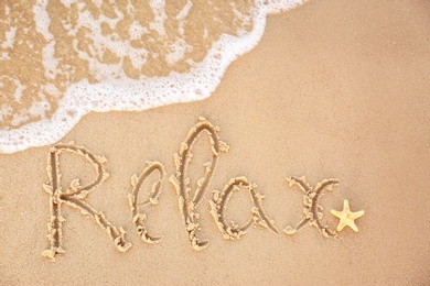 Photo of Word "RELAX" written on sandy beach and sea wave, top view