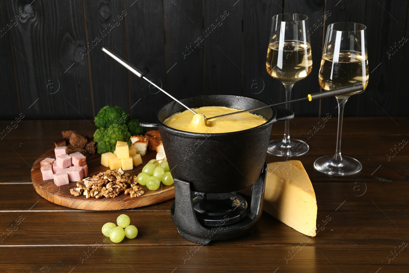 Photo of Fondue pot with melted cheese, glasses of wine and different products on wooden table