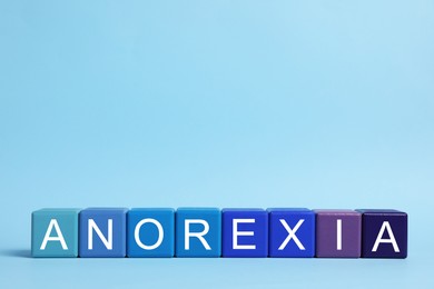 Photo of Word Anorexia made of colorful cubes with letters on light blue background