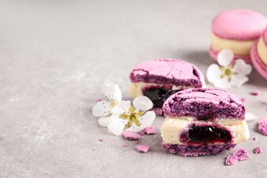 Photo of Halves of delicious violet macaron and flowers on light grey table, space for text