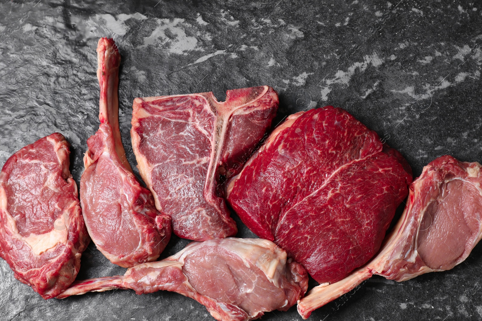 Photo of Fresh raw beef cuts on grey textured table, flat lay