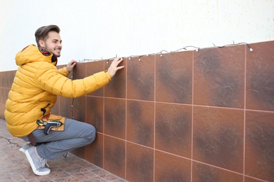 Young man decorating outdoor wall with Christmas lights