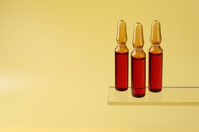 Photo of Glass ampoules with liquid on yellow background. Space for text