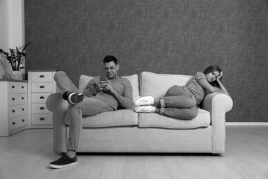 Photo of Man using smartphone and ignoring his girlfriend in room, black and white effect. Loneliness concept