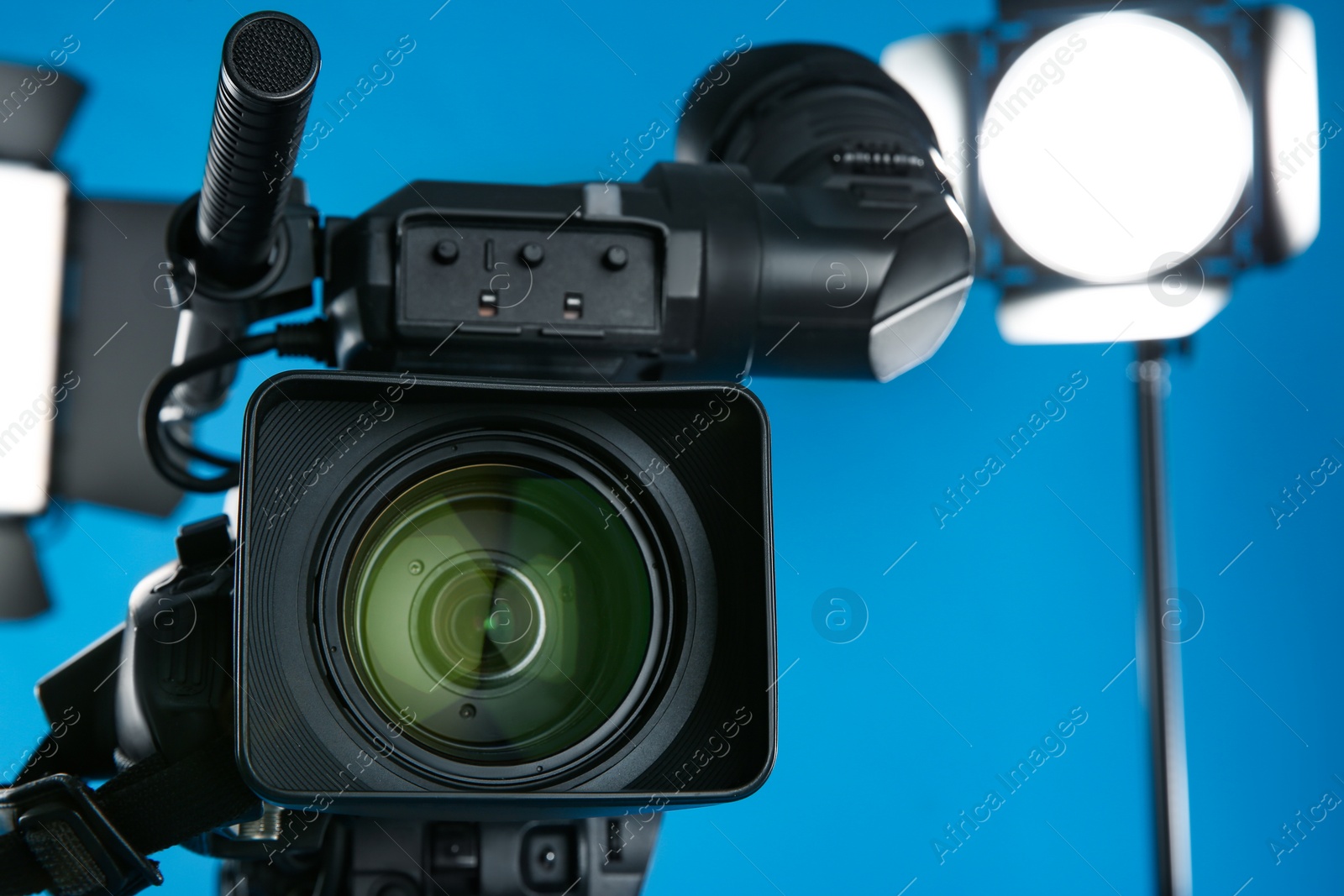 Photo of Professional video camera and lighting equipment on blue background, closeup