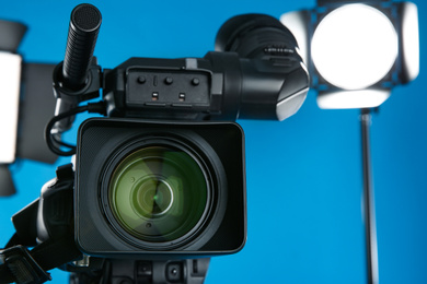 Professional video camera and lighting equipment on blue background, closeup